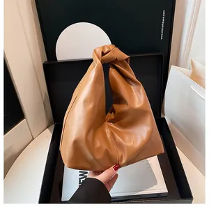 Detail einer braunen Handtasche aus Leder mit geknotetem Griff und modischem Plissee-Design
