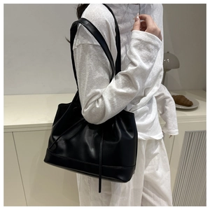 Detail of minimalist black PU leather tote bag with drawstring folds on model