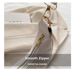 Detail view showing smooth gold zipper and crocodile pattern on beige shoulder bag