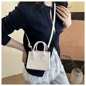 Mini white crossbody bag with crocodile texture worn by model in a minimalist indoor setting
