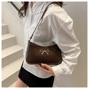 Close-up of a dark brown crocodile-textured underarm bag with a golden bow buckle