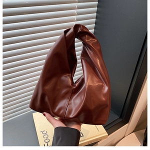 Detail of caramel brown leather bucket bag featuring a unique knotted top handle design