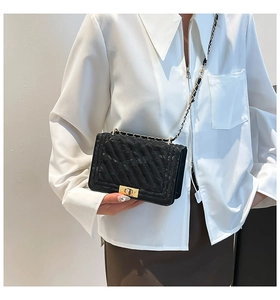 Detail of black crossbody bag featuring gold clasp and leather-woven chain strap