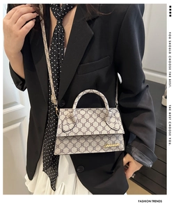 Détail d'un petit sac bandoulière vintage avec logo doré sur un blazer noir chic