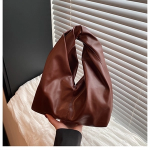Detail of a brown leather handbag with unique knotted handle and pleated bucket design