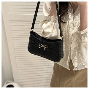 Close-up of black woven leather texture and golden bow buckle on the shoulder bag