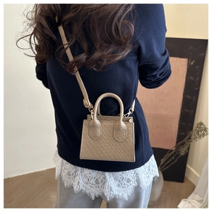 Model wearing a khaki woven mini crossbody bag with a blue sweater and lace detail