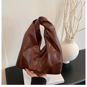 Detail of caramel brown soft leather handbag featuring a unique knotted handle design