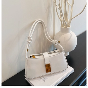 Detailed close-up of white minimalist baguette bag with knot strap and gold hardware accents