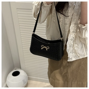 Close-up of black woven underarm bag featuring a delicate gold metal bow ornament