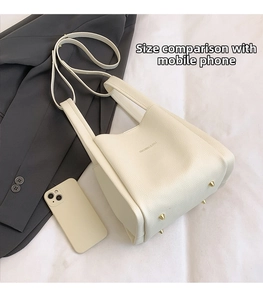 Close-up of white pebble leather bucket bag with gold protective feet and phone for scale