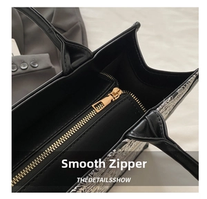 Close-up of the smooth golden metal zipper and embroidery detail on the black tote bag
