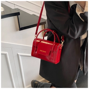 Détail du mini sac rouge en cuir verni avec boucle dorée porté sur un costume noir