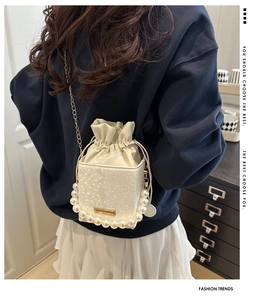 Detail of white snakeskin bucket bag with pearl handle and metal chain strap on model
