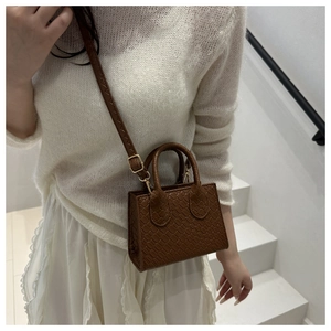 Brown crocodile texture mini tote bag on model's shoulder against a white staircase
