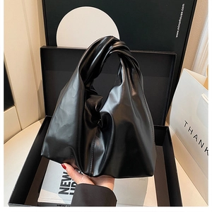 Detail of glossy black bucket bag with elegant knotted handle and pleated texture