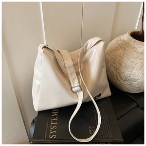 Macro detail of creamy patent leather shoulder bag with metallic logo on a book