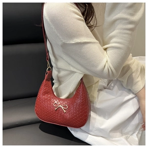 Détail du sac porté épaule rouge tressé avec nœud doré et forme en demi-lune
