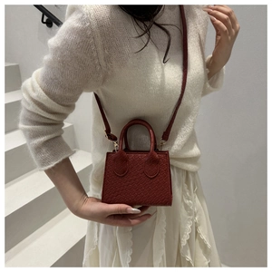 Close-up of woven texture on red-brown mini crossbody bag with metal strap buckle