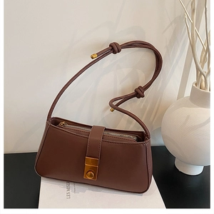 Detailed view of deep brown baguette bag with golden buckle and knotted strap on books