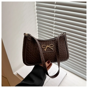 Detail of dark brown woven shoulder bag with a gold bow metal accent and fine texture