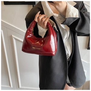 Detail of a dark red patent leather hobo bag with gold logo and premium glossy finish