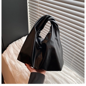 Detail of minimalist black pleated bucket bag featuring a unique knotted top handle design