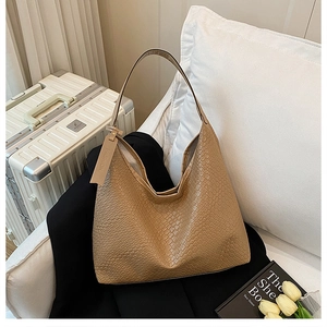 Detail of khaki hobo bag with crocodile texture leaning on blazer and travel suitcase