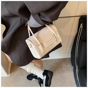 Détail du sac carré en cuir grainé crème avec logo et lettrage doré élégant