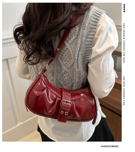 Detail of burgundy ruched faux leather shoulder bag with metallic buckle on a model