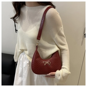 Detail of burgundy crescent shoulder bag featuring woven texture and gold bow pendant