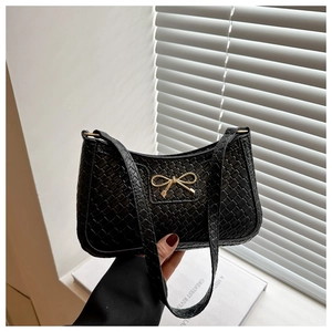 Detail of black woven shoulder bag with a gold metal bow and sleek baguette texture