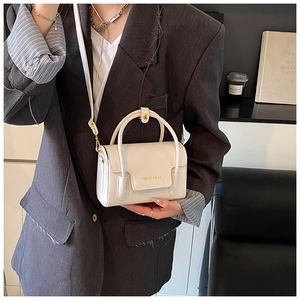 Détail du sac à main en cuir crème avec texte Fashion & Bags sur un blazer gris