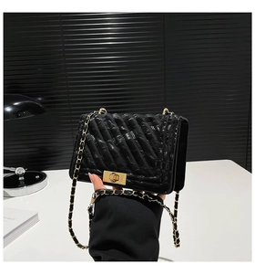 Detail of black quilted leather shoulder bag with gold chain strap and metallic lock clasp