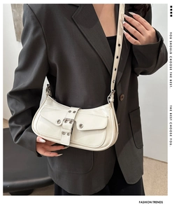 Detail of ivory patent leather shoulder bag with buckle and metallic eyelets on grey blazer