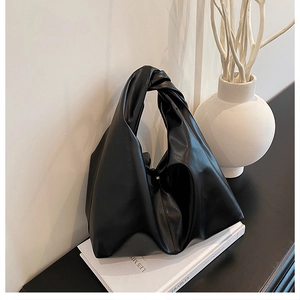 Detail des geknoteten Tragegriffs und der glatten Kunstlederstruktur der schwarzen Tasche