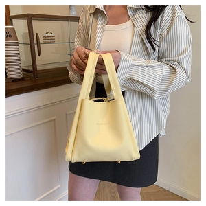 Detail of light yellow bucket bag with lychee grain texture and gold protective feet