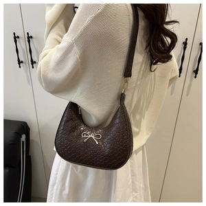 Detail of dark brown woven shoulder bag with golden bow buckle on cream texture outfit
