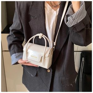 Détail du mini sac carré en cuir crème avec lettrage doré et poignée supérieure fixe