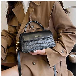 Close-up of black crocodile-embossed leather handbag with gold logo held by a model