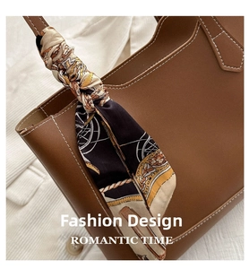 Détail d'un sac cabas en cuir marron avec un foulard en soie imprimé décoratif sur l'anse