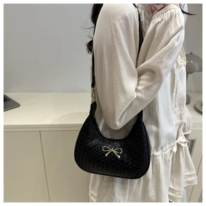 Close-up of black crocodile pattern leather underarm bag with gold bow detail