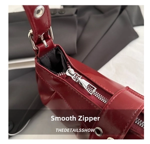 Close-up of smooth silver zipper and metallic eyelets on a red patent leather handbag