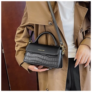 Detail of black faux crocodile skin texture and gold hardware on fashionable crossbody bag