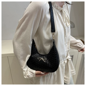 Detail of black leather underarm bag featuring a textured pattern and gold bow charm