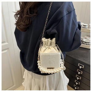 Detailed view of white bucket bag with pearl chain handle and textured leather finish