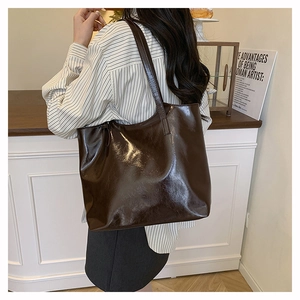 Dettaglio di una grande borsa tote marrone scuro lucido indossata su un outfit