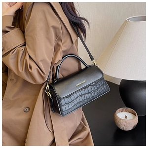Detail view of black crocodile pattern leather handbag with gold hardware and strap