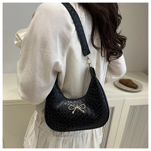 Detailed view of black woven shoulder bag with a gold bow buckle on model