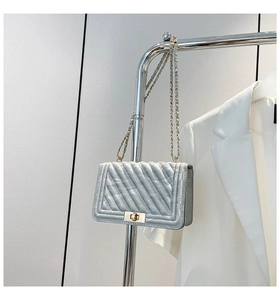 Close-up of silver quilted crossbody bag with metal chain strap and twist lock detail